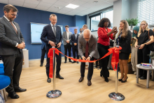 Rektor przecinający wstęgę. Za nim i obok niego stoją pozostali uczestnicy wydarzenia.