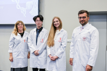 Cztery osoby, kobiety i mężczyźni, stoją w rzędzie w białych fartuchach laboratoryjnych 