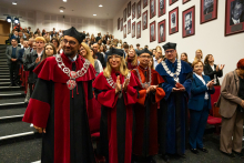 Grupa osób w trakcie uroczystości. Ubrane są w togi akademickie. Uśmiechają się do zdjęcia.