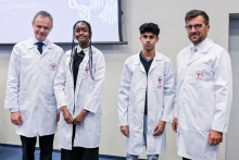 Cztery osoby, kobiety i mężczyźni, stoją w rzędzie w białych fartuchach laboratoryjnych 