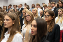 Grupa młodych osób, głównie kobiet w eleganckich ubraniach. W centrum kadru znajdują się dwie kobiety w okularach. 