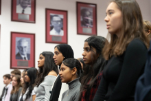 Grupa młodych osób stoi w rzędzie i patrzy w jednym kierunku. Na pierwszym planie widać twarze kilku kobiet o różnych kolorach skóry i włosów.