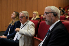 OCztery osoby siedzą w czerwonych fotelach w sali konferencyjnej. Wszystkie mają na sobie słuchawki z mikrofonami, co sugeruje udział w tłumaczeniu symultanicznym