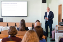 Osoba prowadzi prezentację w sali wykładowej. Na ekranie widoczny slajd o farmakoterapii w ratownictwie medycznym. Na pierwszym planie siedzą słuchacze.