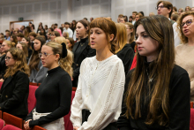 Grupa młodych ludzi w auli. To immatrykulowani studenci. Stoją w rzędach pomiędzy czerwonymi fotelami. Są nieformalnie ubrani. Mają skupione twarze.