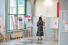 Kobieta stoi przed szeregiem plakatów naukowych umieszczonych na sztalugach w przestronnym, dobrze oświetlonym pomieszczeniu. 