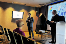 Na sali widać trzy osoby. Jedna z nich, elegancko ubrany mężczyzna - dziekan wydziału, przemawia do mikrofonu.