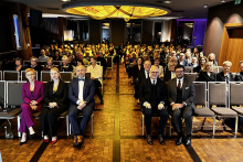 Grupa elegancko ubranych osób. Siedzą na krzesłach w dużej sali. Są to uczestnicy jubileuszu 75-lecia kliniki.