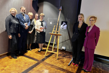 Kilka osób, elegancko ubranych, pozuje przy tablicy upamiętniającej prof. Kossakowskiego.