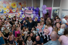 Grupa osób pozująca do zdjęcia. Wszyscy są uśmiechnięci. Za nimi widać fioletowe balony, na ścianach są kolorowe rysunki.