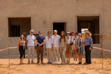 Grupa osób stoi na zewnątrz przed nieotynkowanym budynkiem w trakcie budowy, na ziemi widoczne jest oznaczenie taśmą ostrzegawczą.