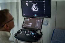 Close-up of an ultrasound machine with two screens. The upper monitor displays a grayscale ultrasound image showing an anatomical cross-section, while the lower screen shows the control panel with the examination settings.