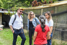 In the photo, four people are standing on the grass near a fenced mesh structure that looks like part of a farm or garden.