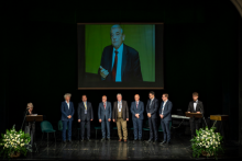A group of elegantly dressed men standing on stage. Behind them, a photo of Prof. Zbigniew Religa can be seen on a multimedia screen.