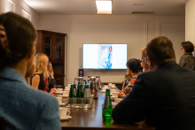 People are sitting at a table in a conference room, watching a presentation on a screen.