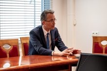 Mężczyzna w czasie spotkania. Jest elegancko ubrany. Opiera ręce o stół. Coś tłumaczy.