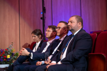 Several people sitting on chairs in an auditorium. They are all elegantly dressed.