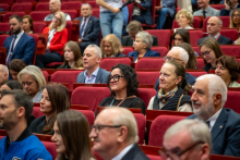 Kilka rzędów osób siedzi w audytorium na czerwonych fotelach podczas konferencji.