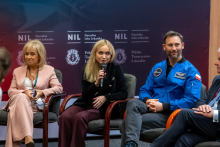 Cztery osoby siedzą na krzesłach w sali konferencyjnej podczas panelu dyskusyjnego. Jedna osoba - ministra zdrowia trzyma mikrofon i przemawia. Wszystkie osoby są elegancko ubrane. W tle widać kolorową ściankę.