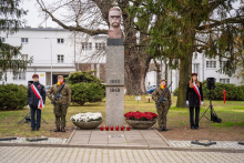 Grupa osób stojących przy marmurowym pomniku z podobizną marszałka Józefa Piłsudskiego.