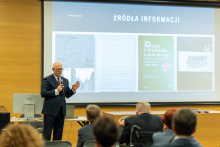 Prof. Rafał Krenke przemawia i pokazuje slajdy na dużym ekranie multimedialnym.