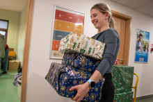 Młoda dziewczyna niosąca trzy paczki zapakowane w biały i niebieski papier.