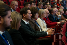 Grupa osób siedzących na auli. Patrzą przed siebie w skupieniu.