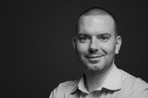 Dr Tomasz Solecki. Młody mężczyzna w koszuli, uśmiecha się do zdjęcia. Fotografia jest czarno-biała.