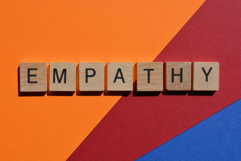 Wooden blocks with letters forming the word “EMPATHY” arranged on a background of triangles in orange, red and blue.