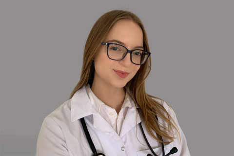 Osoba w białym fartuchu lekarskim ze stetoskopem na szyi, na szarym tle. 