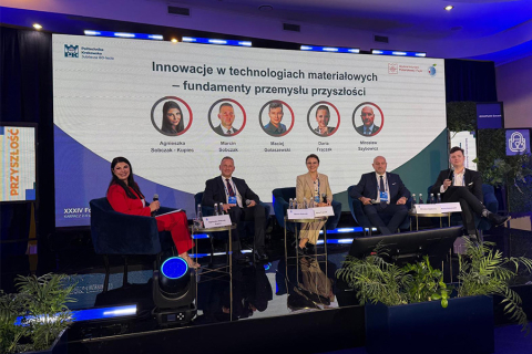 Pięć osób - uczestników panelu dyskusyjnego, siedzi na stronie. Wszyscy są elegancko ubrani. Uśmiechają się do zdjęcia. Za nimi stoi ekran multimedialny, na którym są wyświetlone ich zdjęcia z podpisami oraz tytuł panelu „Innowacje w technologiach materiałowych – fundamenty przemysłu przyszłości”.