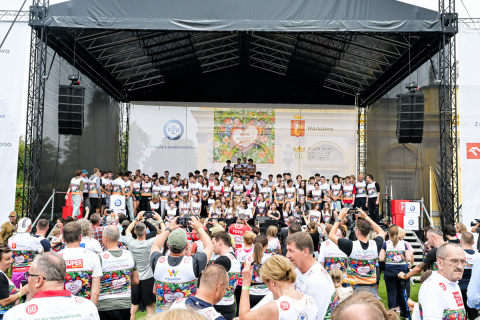 Na scenie stoi około 30 osób. Są ubrane w sportowe stroje i w koszulki z numerami startowymi. Przed sceną stoi tłum ludzi, część robi zdjęcia.
