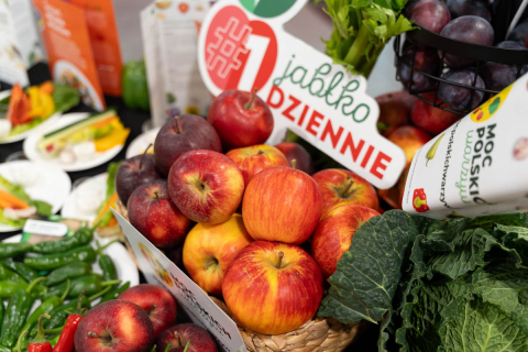 Kosz wypełniony czerwonymi i żółtymi jabłkami otoczony zieloną papryką, liściastymi warzywami i innymi produktami roślinnymi.