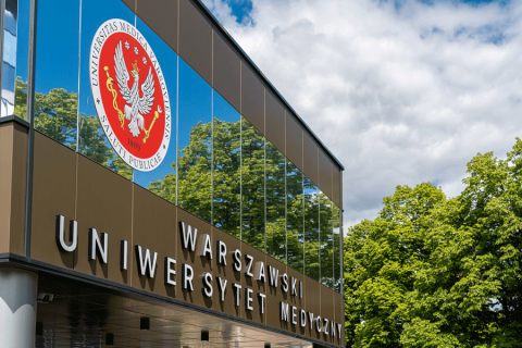 Budynek rektoratu. Budynek koloru szarego, z przeszkloną fasadą, nad nim słońce, które odbija się od szyb.