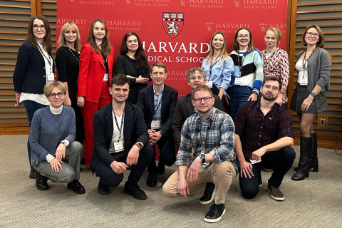 A group of people in a conference room in front of a red background with the Harvard Medical School logo and the repeated inscription “Harvard Medical School.” 