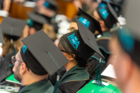 Dyplomowani sfotografowani od tyłu, widać birety na ich głowach z logotypem studiów MBA.