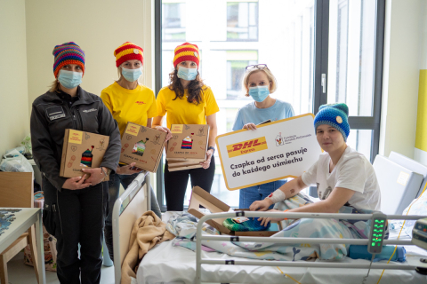 In a hospital room, a group of people give colorful woolen hats to a teenage patient.